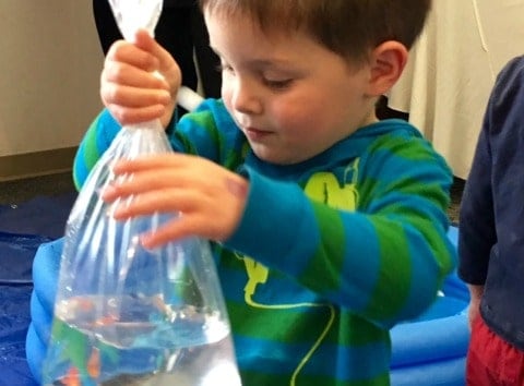 a young boy holding a plastic spoon and a plastic bag filled with water.