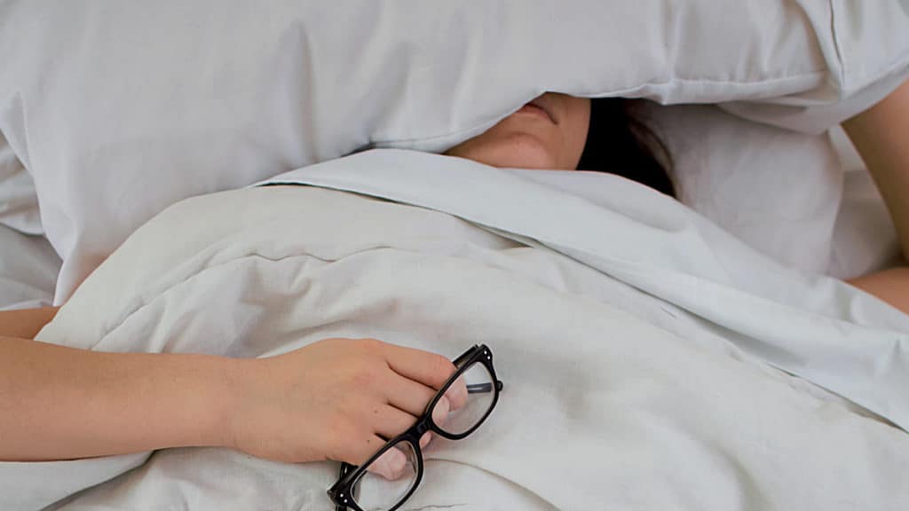 a woman laying in bed with a pair of glasses.