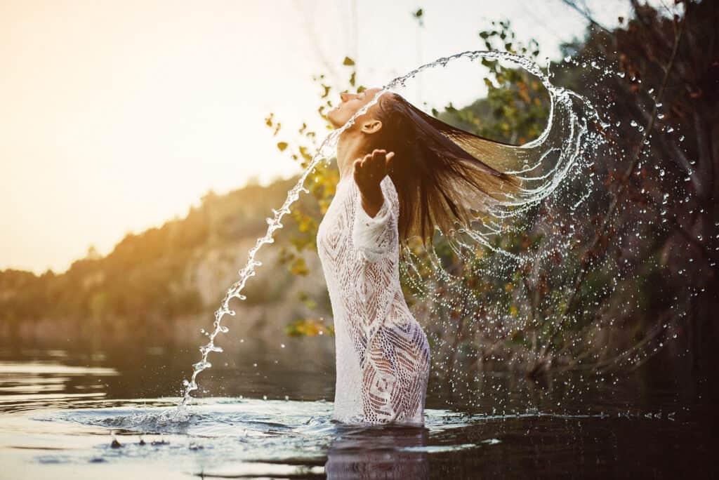 Avoid Ac in the summer a woman standing in a body of water with her hair in the air.