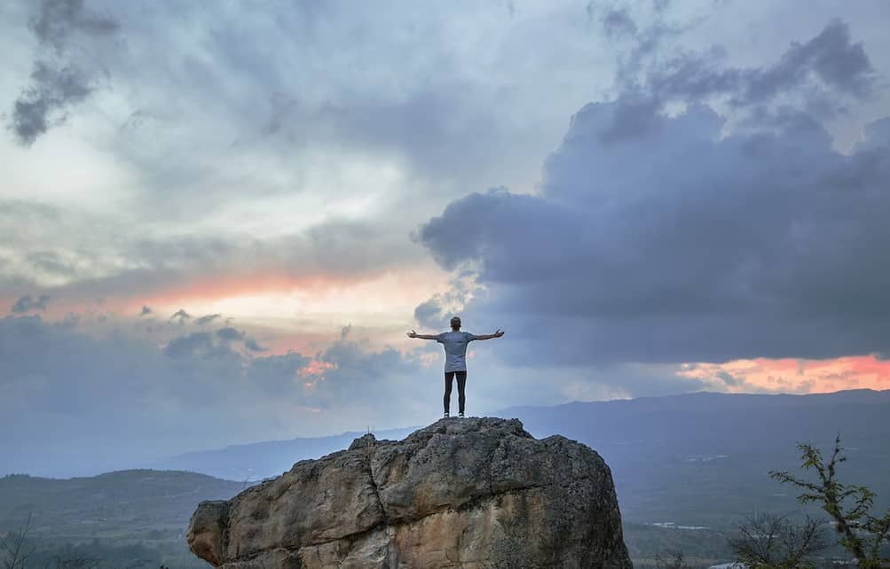 a man standing on a rock with his arms out.