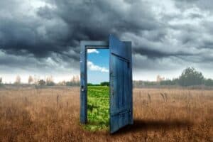 An open door in a field with a stormy sky.