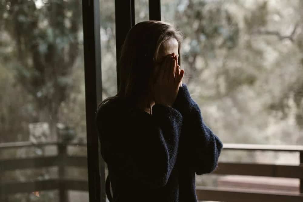 A woman covering her face in front of a window.