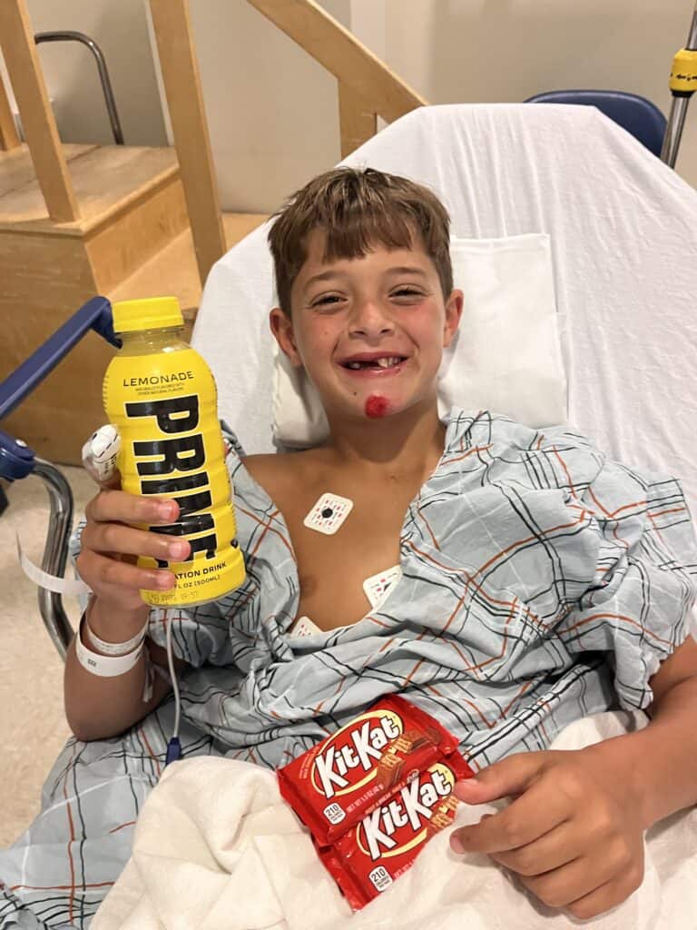 A boy in a hospital bed holding a bottle of krups.