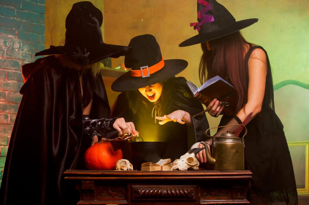 Three witches making a potion at a table.