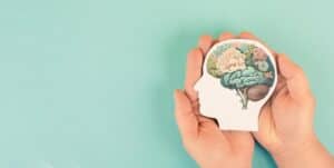 A woman's hand holding a paper brain with flowers on it.