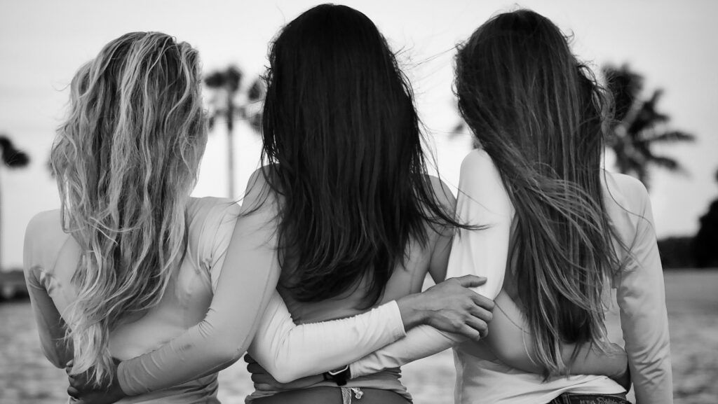 A black and white photo of three women hugging on the beach.