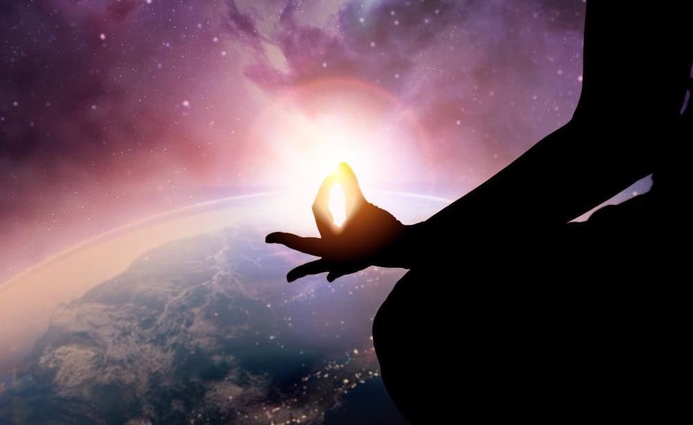 Silhouette of a person meditating in a lotus position against a cosmic background with Earth and a glowing light.