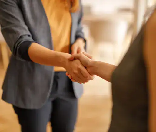 Two people are shaking hands in an indoor setting. Only their torsos and arms are visible.