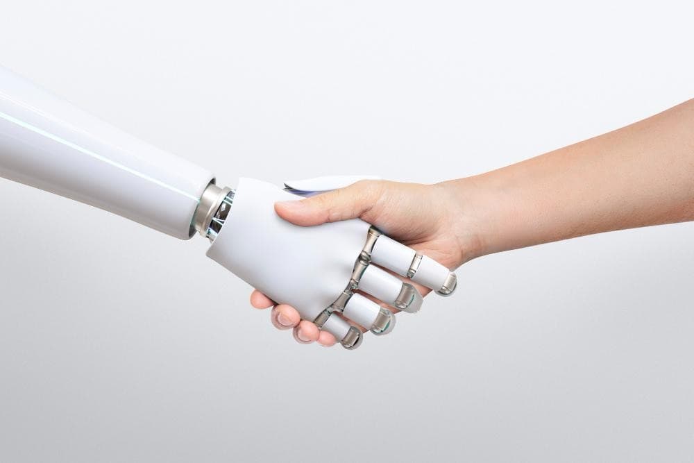 When Coaching Gets Digital: Using AI to Improve Human Connection 2 A human hand shakes hands with a robotic hand against a plain white background.