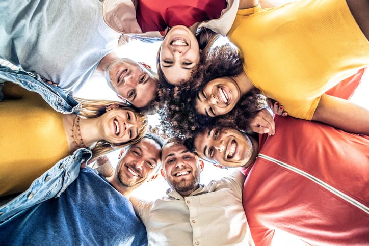 A group of eight people standing in a circle, looking down and smiling at the camera, taken from a low angle.
