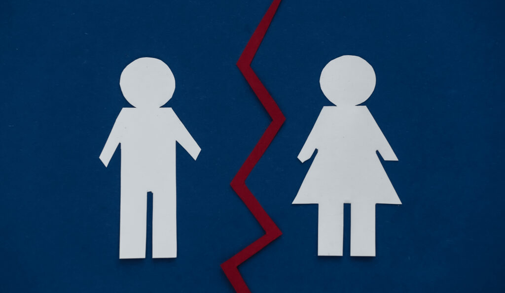 Is Divorce a Second Puberty? 2 Paper cutouts of a man and a woman are separated by a jagged red line on a blue background.